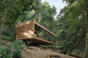 this-wood-covered-house-hovers-above-the-hillside-in-the-forest