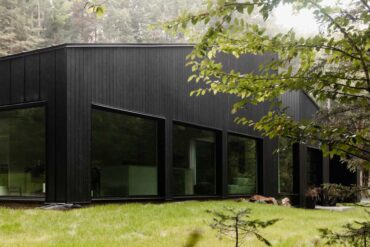 the-black-exterior-of-this-home-in-the-forest-covers-a-white-minimalist-interior